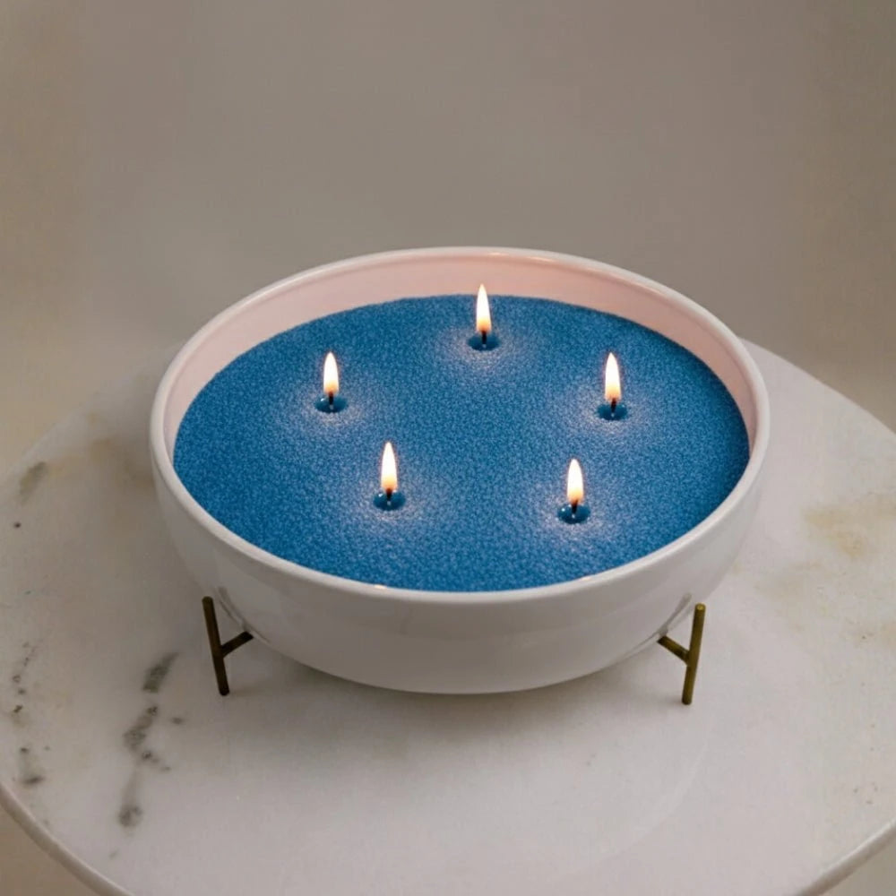 Blue Warmnest candle sand refill burning with five wicks in a white bowl on a marble table