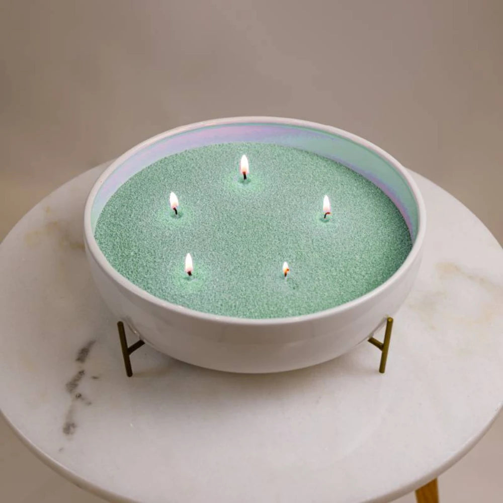 Sage green Warmnest candle sand refill burning with five wicks in a white bowl on a marble table