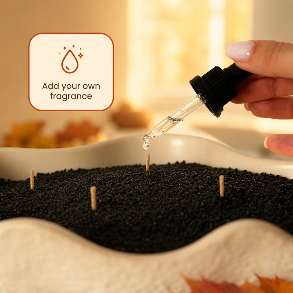 Adding essential oil with a glass dropper to black Warmnest candle sand in a wavy ceramic dish