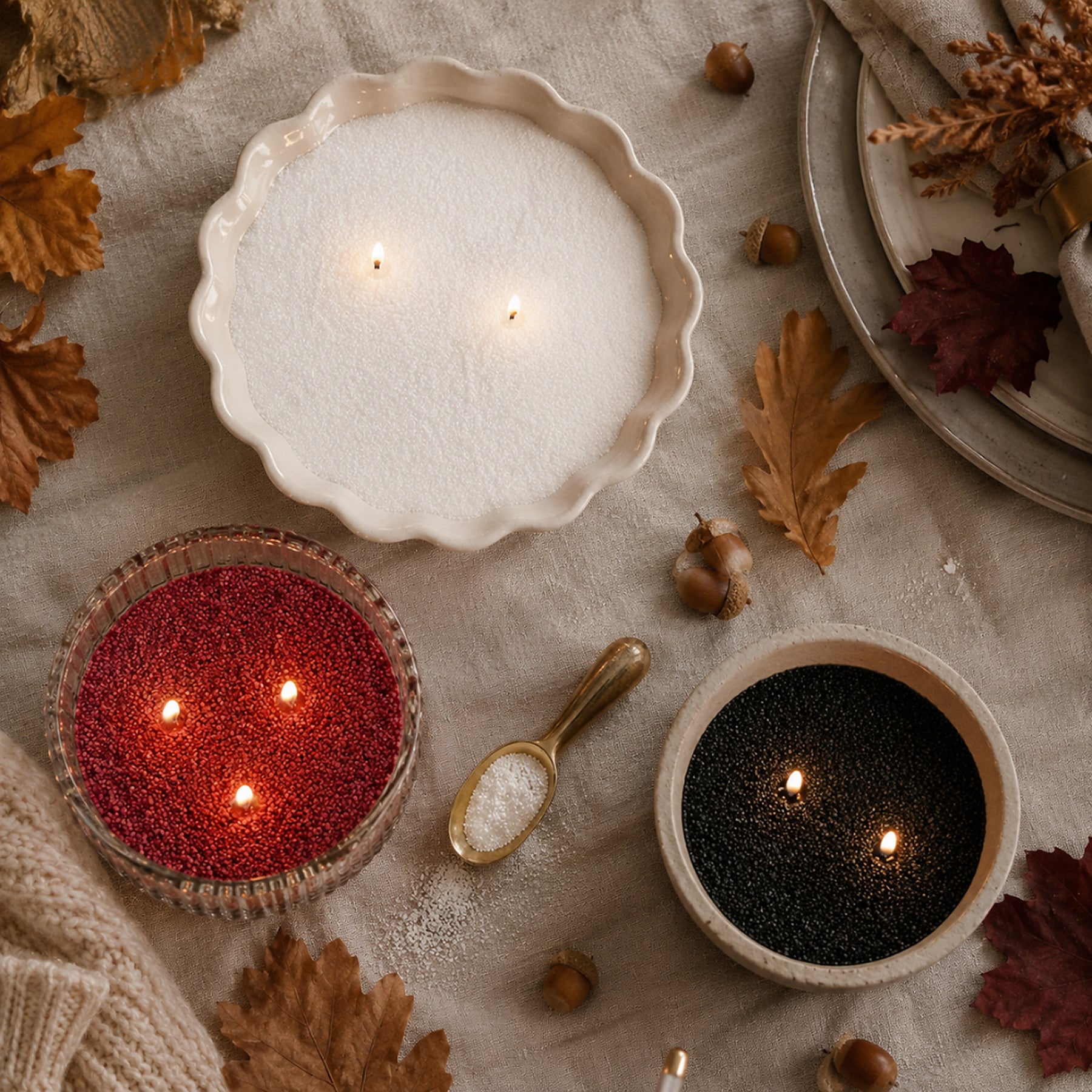 Three pearled candles in white, red and black, on a linen table with autumn leaves and acorns