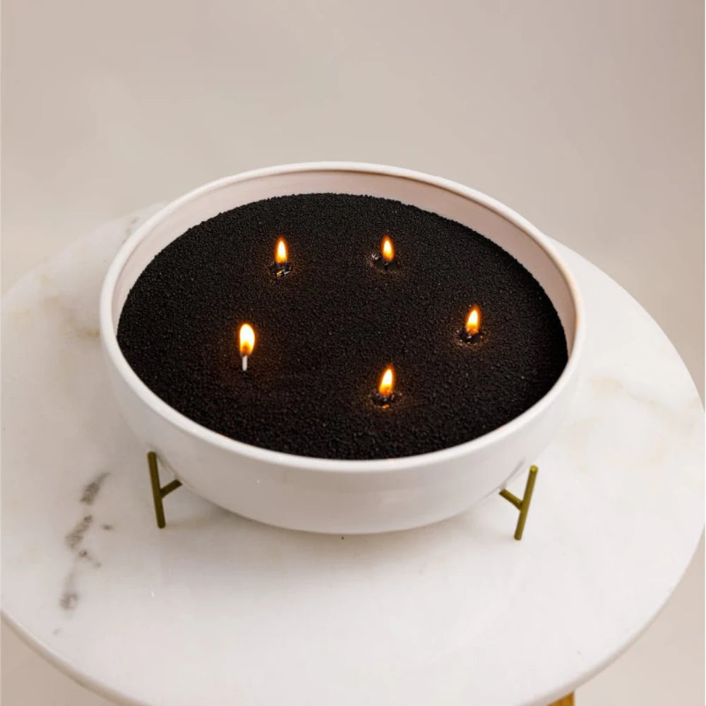 Black Warmnest candle sand refill burning with five wicks in a white bowl on a marble table