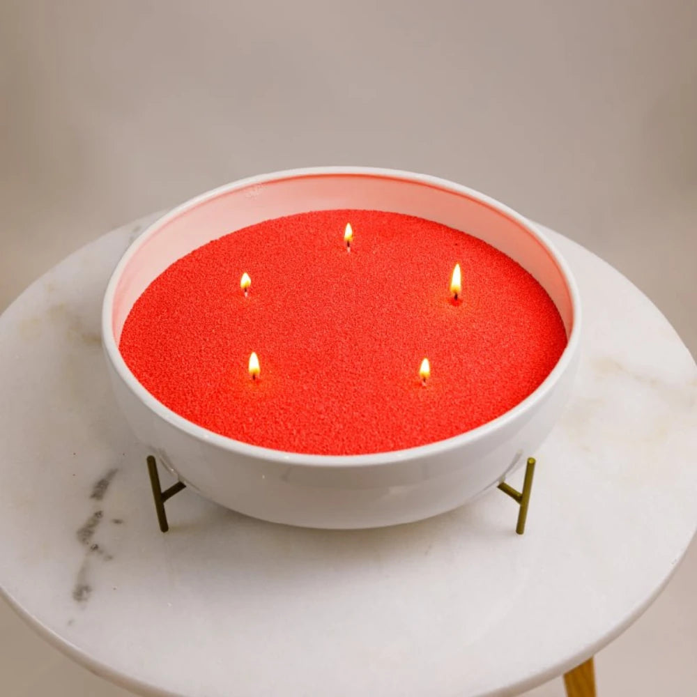 Red Warmnest candle sand refill burning with five wicks in a white bowl on a marble table