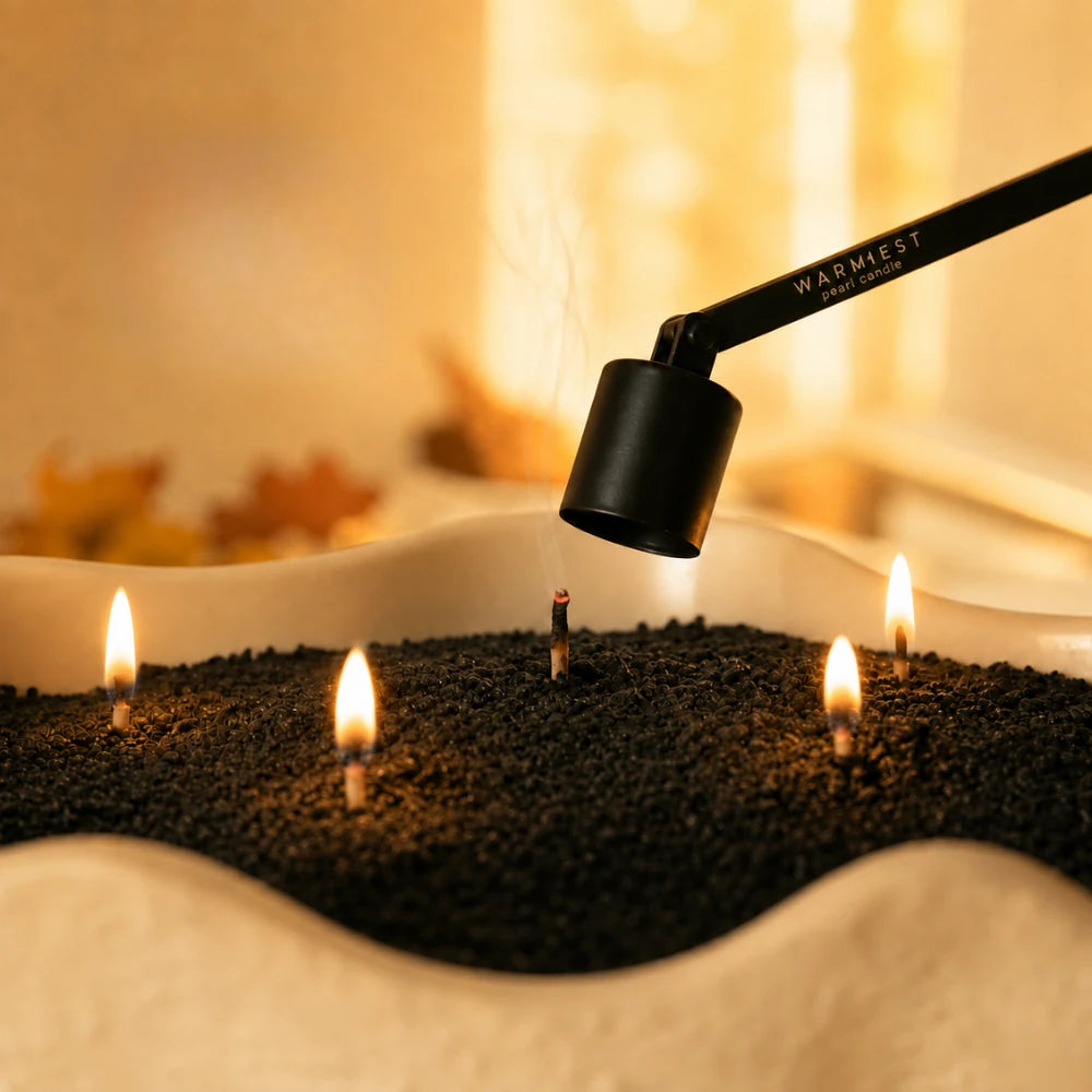 The matte black Warmnest candle snuffer lowered over a wick to extinguish it without smoke, in a dish of black candle sand